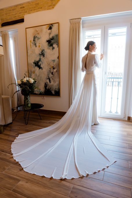 Carla luce un vestido de novia precioso ante la ventana de su casa, en castilleja de la cuesta. sevilla